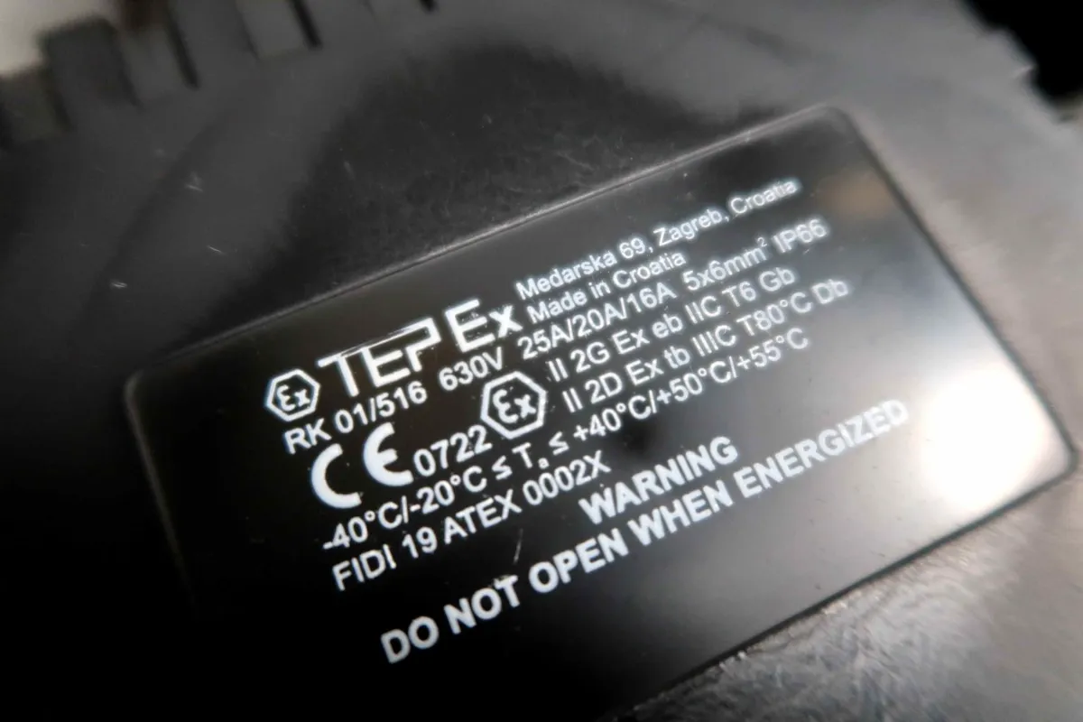 Close-up van een zwart typeplaatje met technische gegevens zoals spanning, temperatuurbereiken, keurmerken en een waarschuwing: Niet openen wanneer het apparaat onder spanning staat.