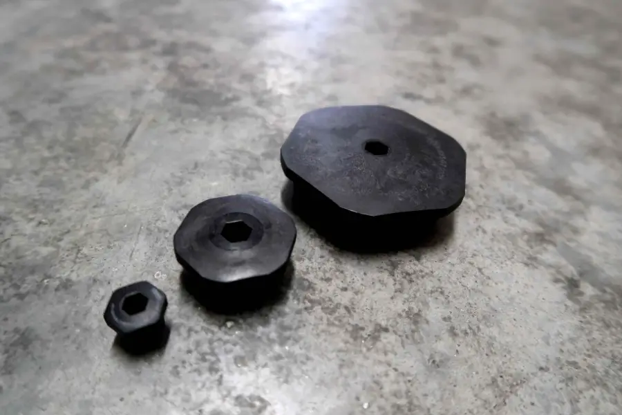 Drie zwarte, achthoekige metalen ringen van verschillende afmetingen liggen op een betonnen oppervlak, van links naar rechts gerangschikt van de kleinste naar de grootste.