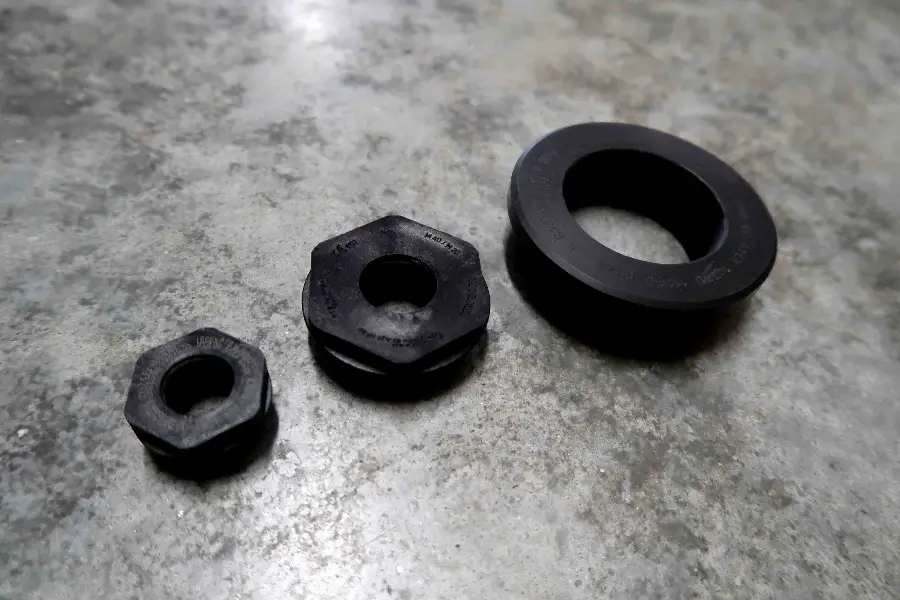 Drie zwarte metalen zeshoekige moeren van verschillende afmetingen liggen naast elkaar op een grijs oppervlak met structuur.