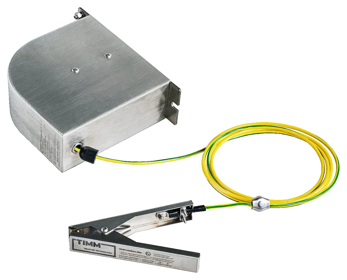 Een metalen aardingsklem met een geelgroene kabel die is bevestigd aan een rechthoekige zilveren doos, bedoeld voor de beveiliging tegen statische ontlading in industriële omgevingen.