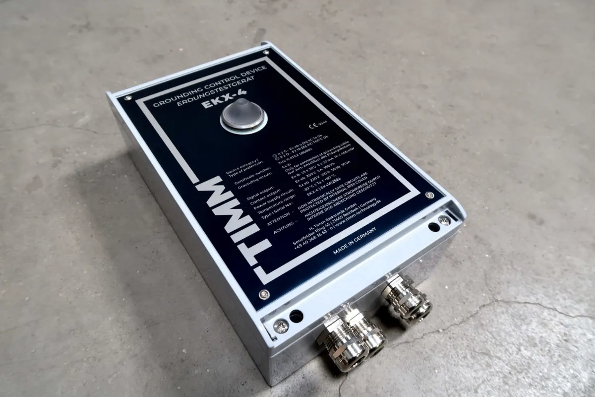 Een TIMM EKX-4-aardingsregelaar met een donkerblauw voorpaneel en twee metalen kabelaansluitingen, geplaatst op een betonnen vloer.