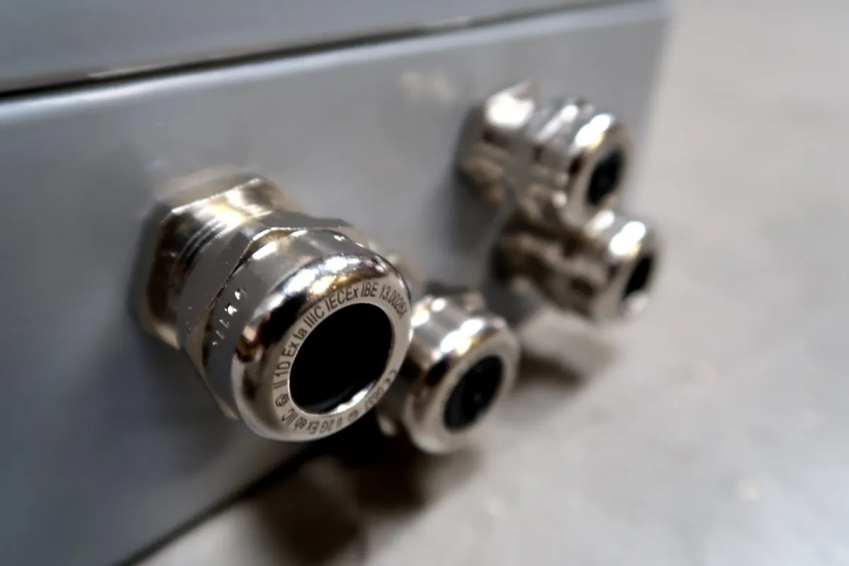 Close-up van vier metalen kabelwartels die op een grijs metalen paneel zijn bevestigd; deze worden vaak gebruikt om elektrische kabels die een behuizing binnenkomen vast te zetten en te beschermen.