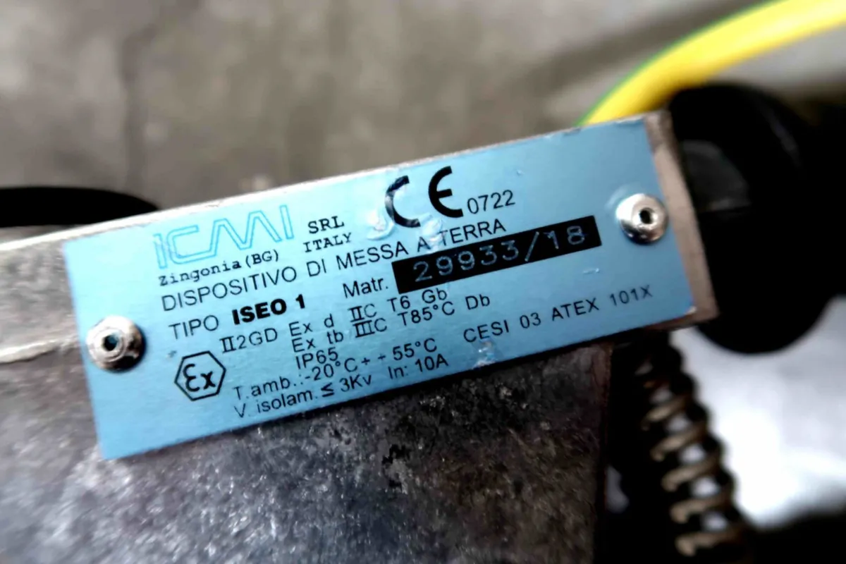 Een close-up van een metalen label op een industrieel apparaat, waarop technische specificaties, certificaten en serienummers staan vermeld, met op de achtergrond enkele draden.