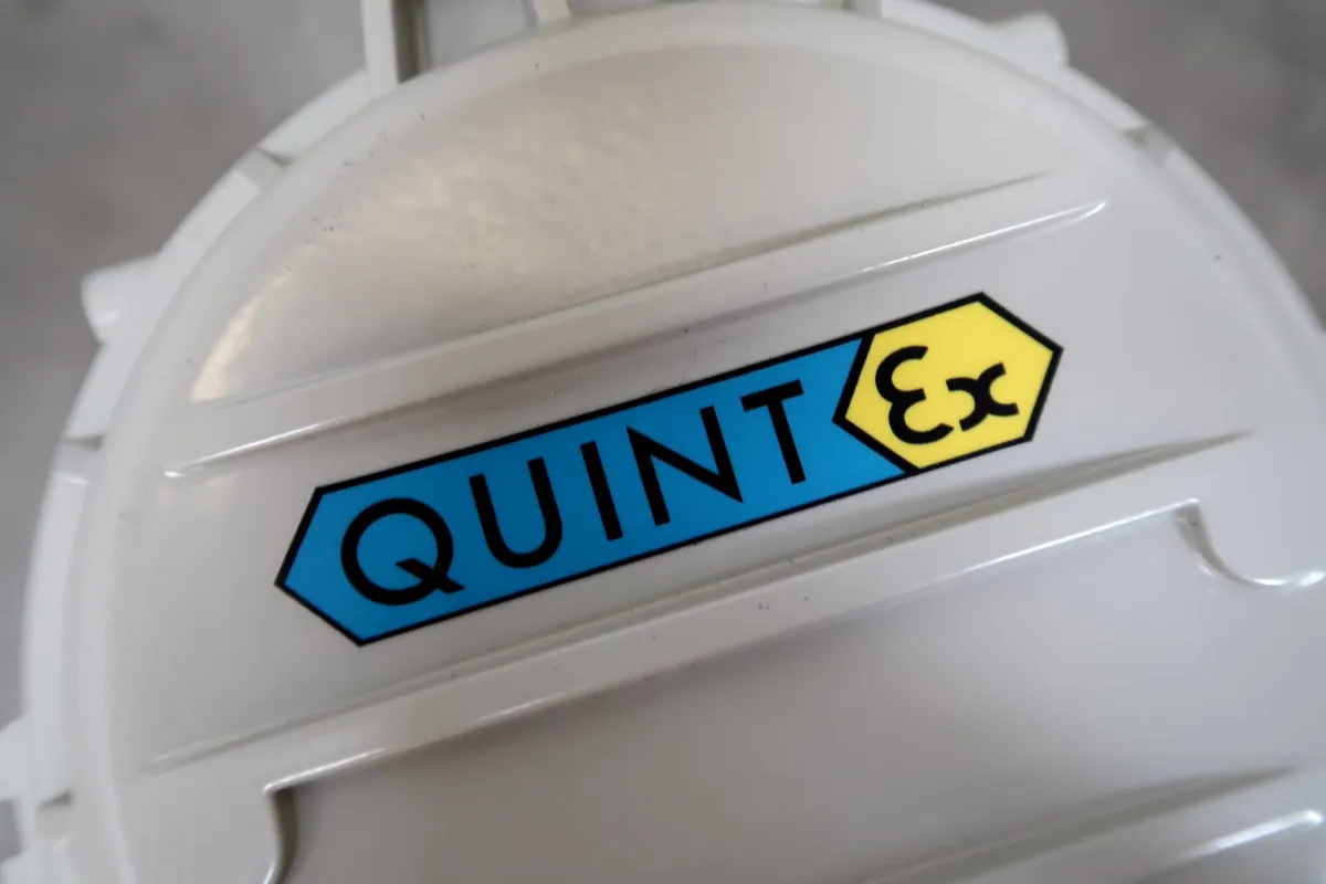 Close-up van een wit apparaat met het opschrift ‘QUINT’ in een blauwe zeshoek en ‘Ex’ in een gele zeshoek, wat erop wijst dat het waarschijnlijk om een explosieveilige industriële component gaat.