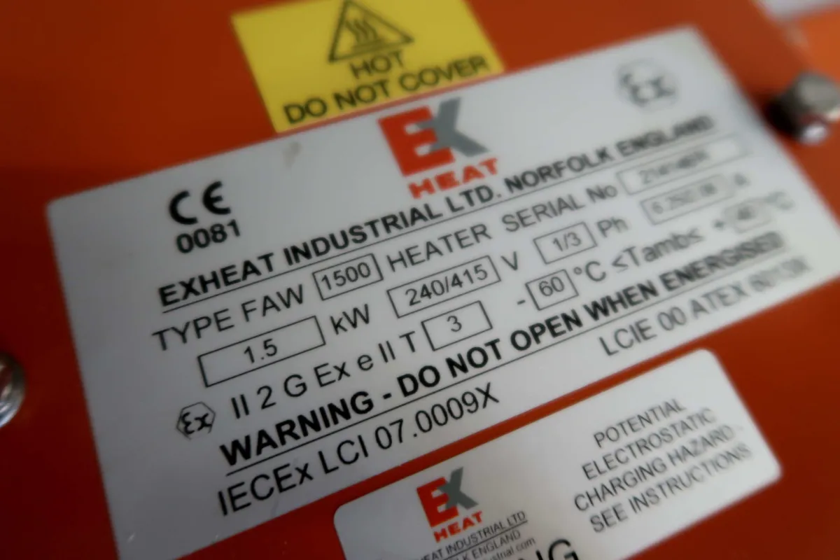 Close-up van een apparaatlabel met technische specificaties en waarschuwingen, zoals ‘NIET OPENEN TIJDENS STROOMTOEVOER’, gegevens over de stroomvoorziening en informatie over de fabrikant EXHEAT Industrial Ltd.