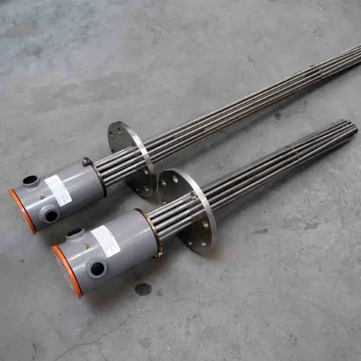 Twee metalen industriële dompelverwarmers met flenzen en cilindervormige schakelkasten, die parallel op een grijze betonnen vloer liggen.