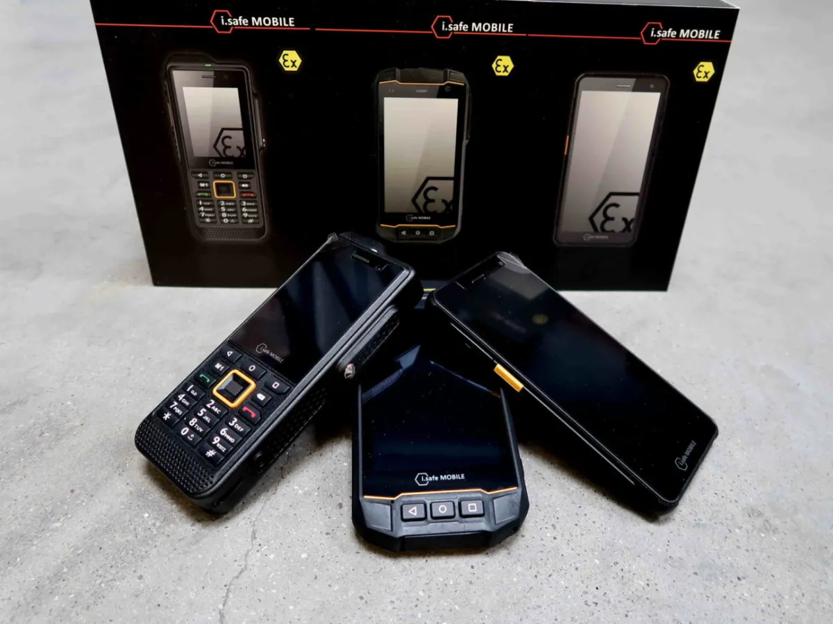 Op een grijs oppervlak staan drie robuuste mobiele telefoons uitgestald, met op de achtergrond de verpakking ervan, waarop afbeeldingen en het merklogo van elk telefoonmodel te zien zijn.