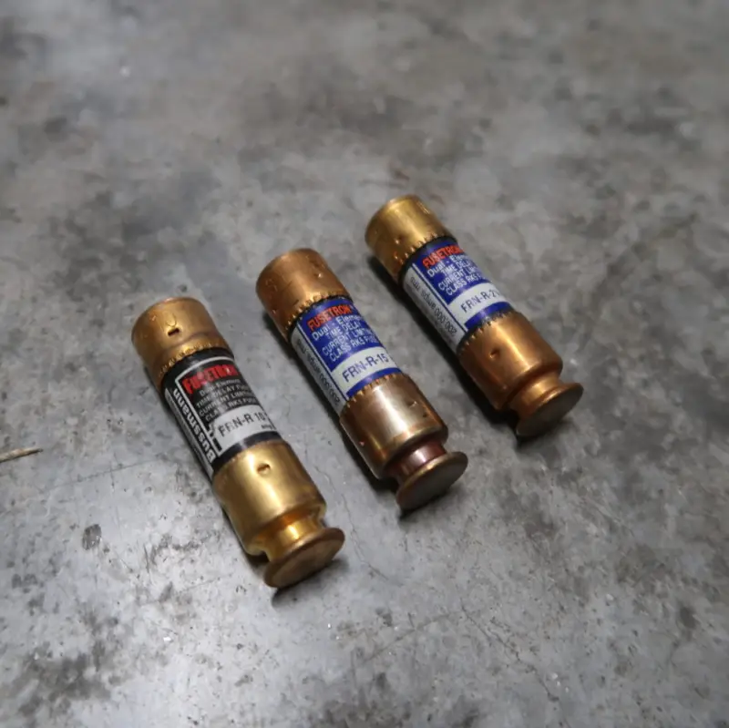 Drie patroonzekeringen met metalen uiteinden en stickers met opschriften liggen op een grijs, enigszins versleten betonnen oppervlak.