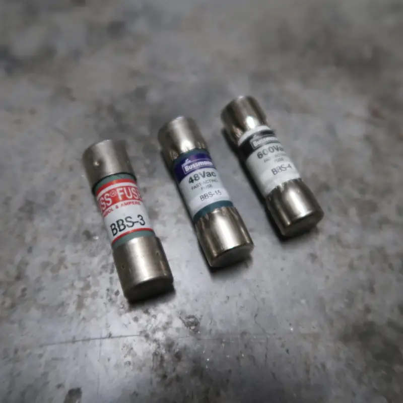 Drie cilindervormige glazen zekeringen met metalen uiteinden liggen op een grijs, gespikkeld oppervlak. Elke zekering is voorzien van een etiket met informatie over de spanning en stroomsterkte.