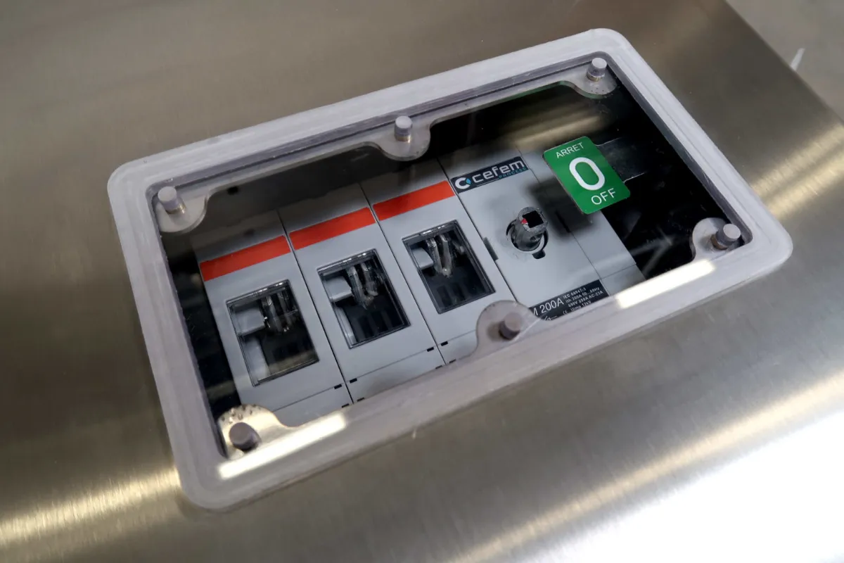 Een close-up van een elektriciteitskast met vier stroomonderbrekers, waarvan er één het opschrift ‘Cefem’ draagt en een andere een groene schakelaar heeft die op 0 OFF staat, gezien door een doorzichtige afdekking.