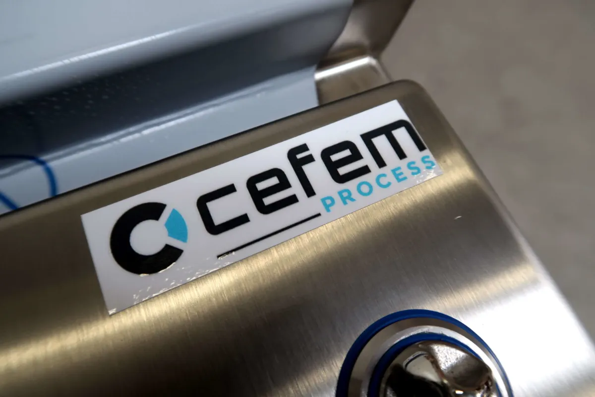 Op een metalen oppervlak vlakbij een sleutelgat is een sticker aangebracht met het logo en de tekst ‘cefem PROCESS’. De achtergrond lijkt deel uit te maken van industriële apparatuur.