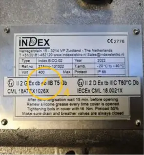 Op een metalen typeplaatje staan technische specificaties vermeld, waaronder spanning, vermogen en het bouwjaar. In een gele cirkel zijn enkele certificeringscodes en classificaties gemarkeerd, met tekst over het gebruik van smeermiddel en het aandraaien van bouten.