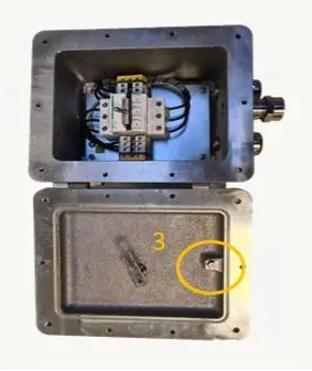 Open metalen aansluitdoos waarin de bedrading zichtbaar is, met het deksel volledig open. Het deksel is voorzien van een scharnier en een klein sluitje, gemarkeerd door een gele cirkel met daarnaast het cijfer 3.