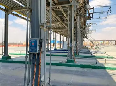 Een industriële constructie met rijen metalen buizen, ladders en bedieningspanelen op een betonnen ondergrond, tegen een achtergrond van een blauwe lucht met hier en daar wat wolken. Het gebied lijkt deel uit te maken van een verwerkings- of opslagfaciliteit.