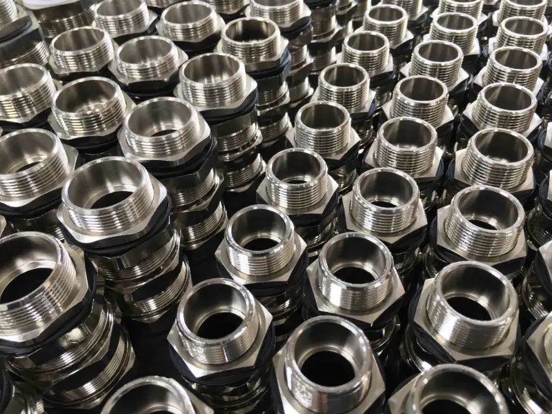 Rijen glanzende, zeshoekige metalen buisfittingen met schroefdraadopeningen zijn netjes gerangschikt in een zich herhalend patroon, waardoor een industriële en overzichtelijke uitstraling ontstaat.