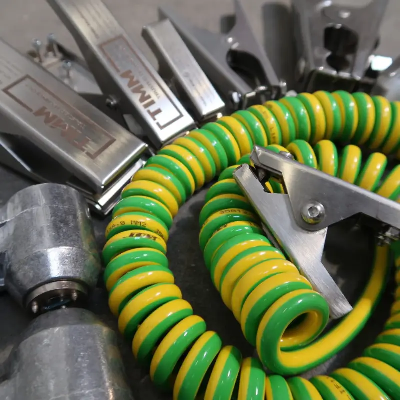 Close-up van een geel-groene spiraalkabel met een metalen klem, omringd door metalen gereedschappen en onderdelen op een grijs oppervlak.