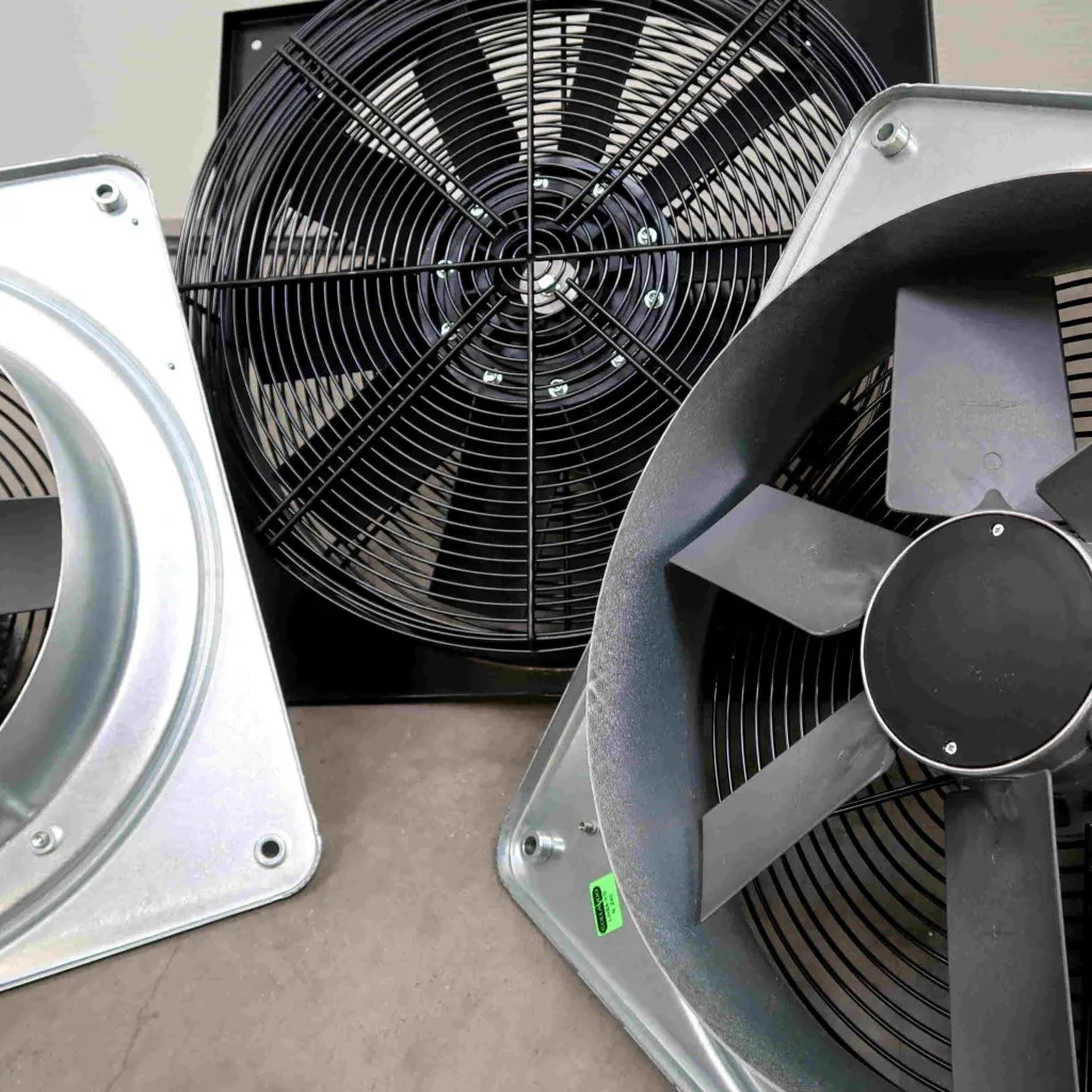 Drie industriële ventilatoren met metalen bladen en beschermroosters staan op een grijs oppervlak, waarbij ze elkaar gedeeltelijk overlappen; gezien van bovenaf onder een hoek.