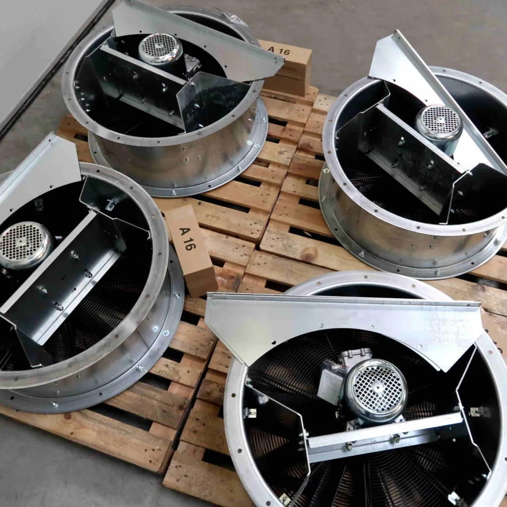 Vier grote industriële ventilatoren met metalen behuizingen staan op houten pallets. Naast de ventilatoren staan twee kartonnen dozen met het opschrift A 16 op een gladde betonnen vloer.
