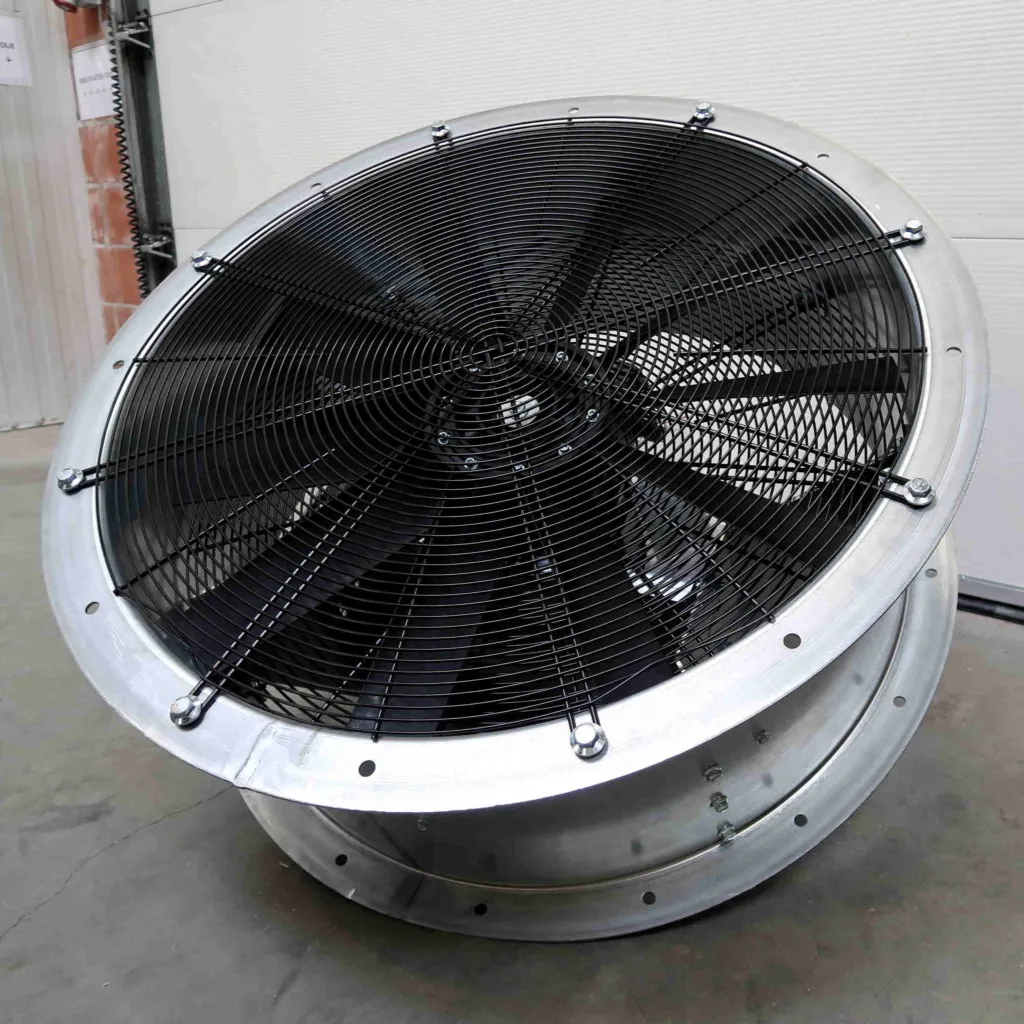 Grote industriële ventilator met een metalen frame en een zwart beschermrooster, geplaatst op een betonnen vloer in een gebouw of magazijn.