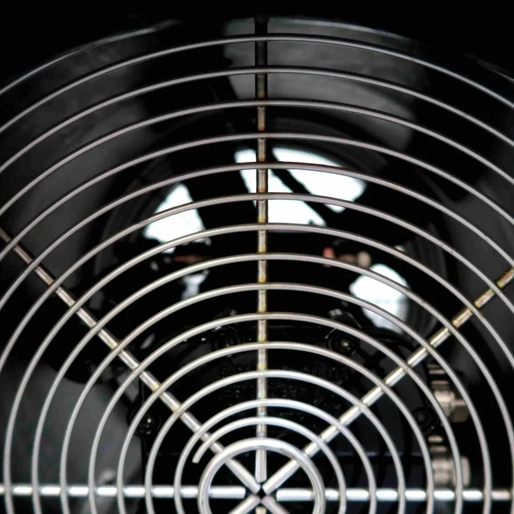 Close-up van een ronde metalen ventilatorbeschermkap met cirkelvormige roosterlijnen, die de bladen van een elektrische ventilator of industriële ventilator beschermt, gezien vanaf de voorkant.