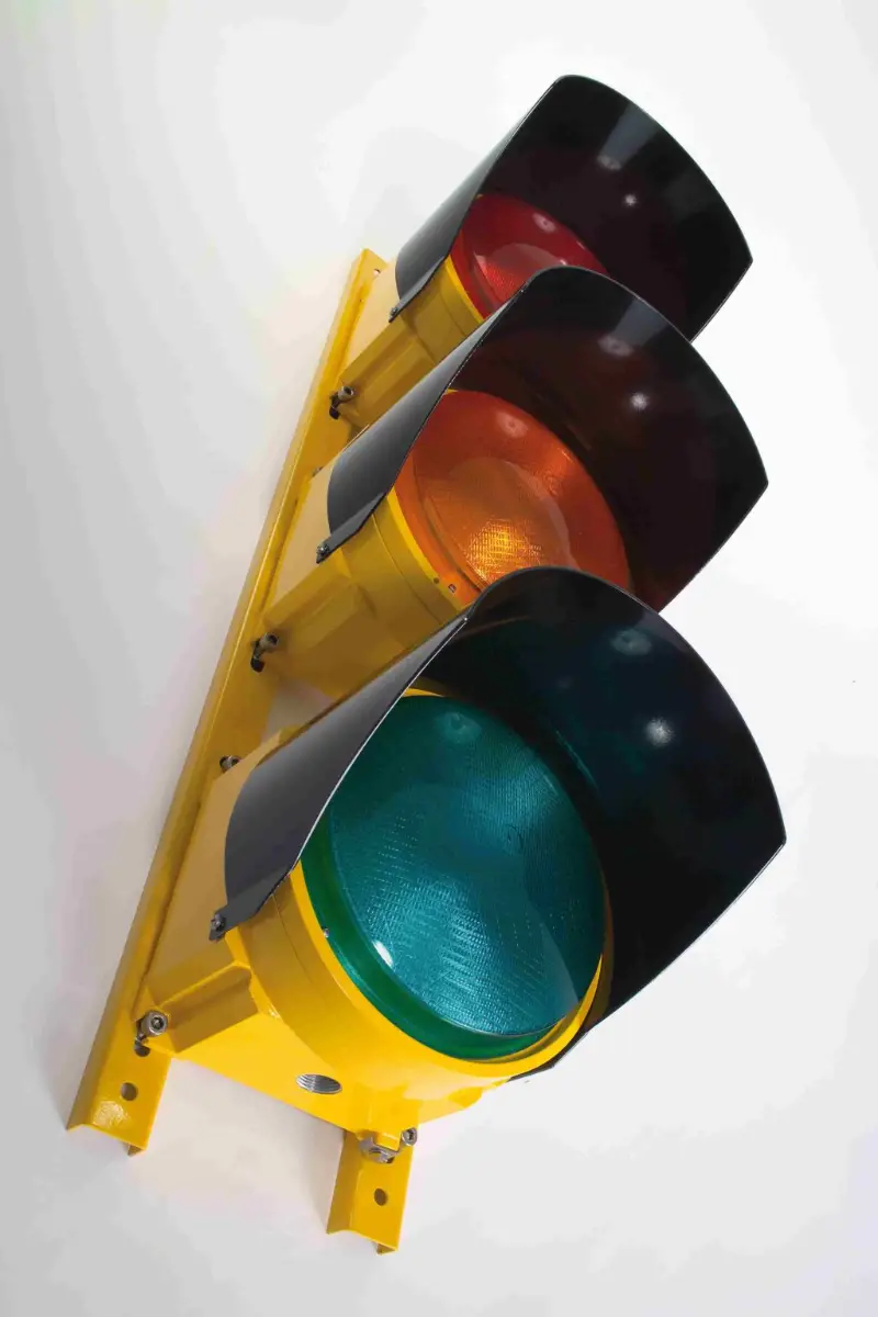 Een op een geel paneel gemonteerd verkeerslicht, gezien vanuit een hoek, met groene, gele en rode lampen waarvan de lenzen gedeeltelijk door schaduwen worden bedekt.