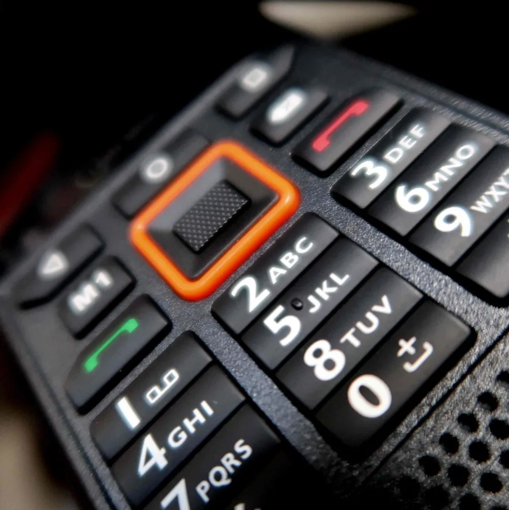 Close-up van een zwart toetsenblok op een oude mobiele telefoon, met cijfer- en lettertoetsen en een centrale navigatietoets met een rode omtrek.
