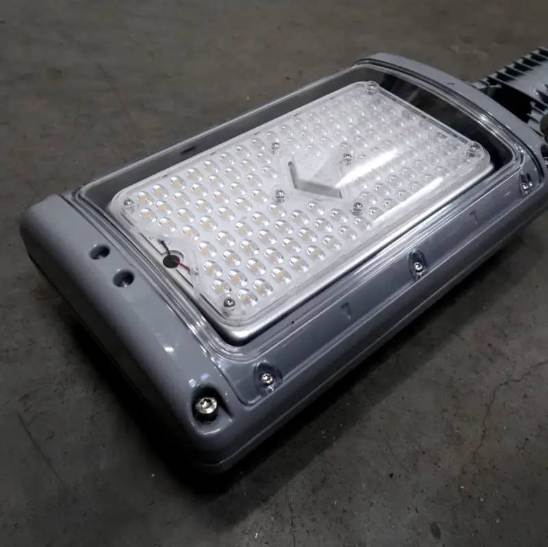 Een close-up van een grijze LED-straatlantaarn die op een betonnen vloer ligt, waarop de rechthoekige opstelling van kleine LED-lampjes onder een doorzichtige beschermkap te zien is.