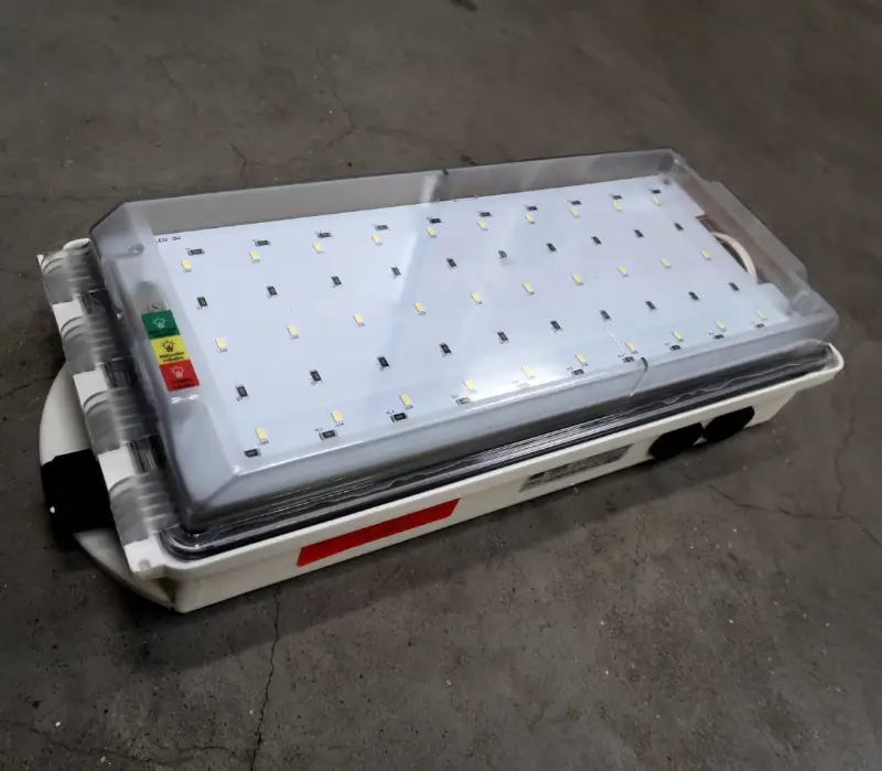 Op een betonnen vloer ligt een rechthoekige LED-lamp met een doorzichtige kap, bedieningsknoppen en een indicatiedisplay.