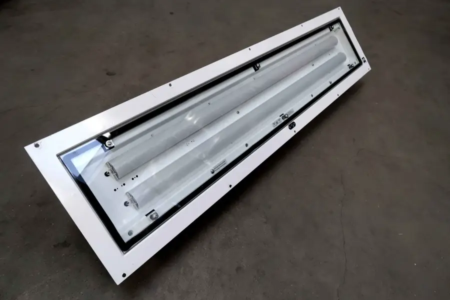 Een rechthoekige tl-armatuur in industriële stijl met een wit frame en een doorzichtige kap, geplaatst op een grijze betonnen vloer.