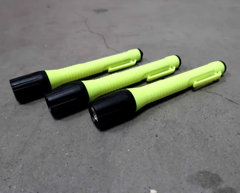 Drie geel-zwarte zaklampen met een klem zitten naast elkaar op een grijs betonnen oppervlak.