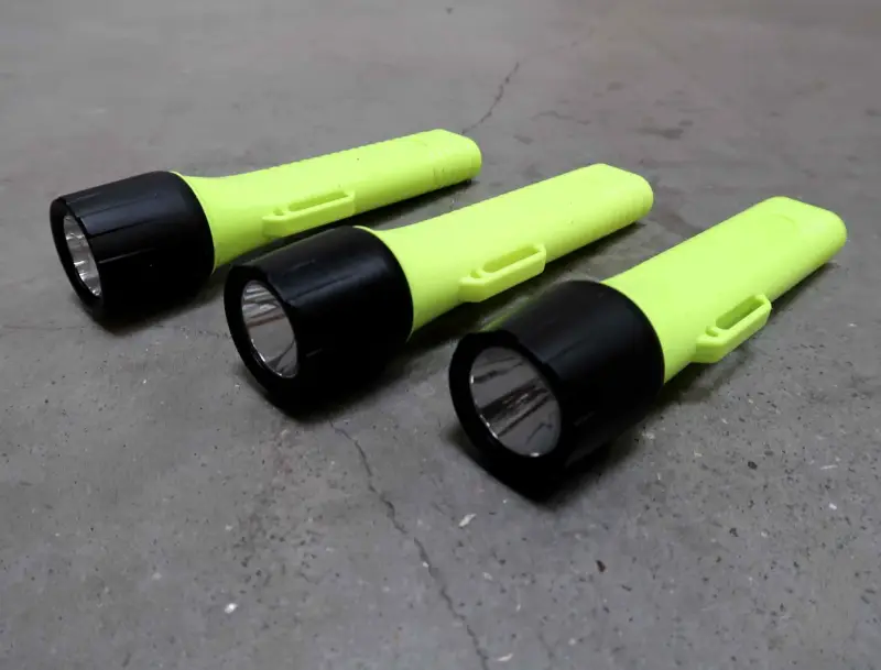 Er liggen drie gele zaklampen met zwarte koppen op een grijs betonnen oppervlak, naast elkaar geplaatst en lichtjes van elkaar af gericht.