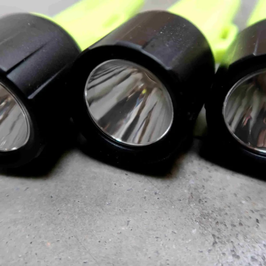 Drie zwart-gele zaklampen liggen naast elkaar op een grijs oppervlak; ze zijn van dichtbij van voren gefotografeerd, zodat hun reflecterende lenzen goed te zien zijn.