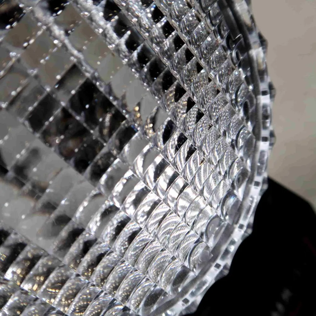 Close-up van een gestructureerd, transparant oppervlak, mogelijk glas of acryl, met een kruispatroon dat het licht weerkaatst en een geometrisch, mozaïekachtig effect creëert.
