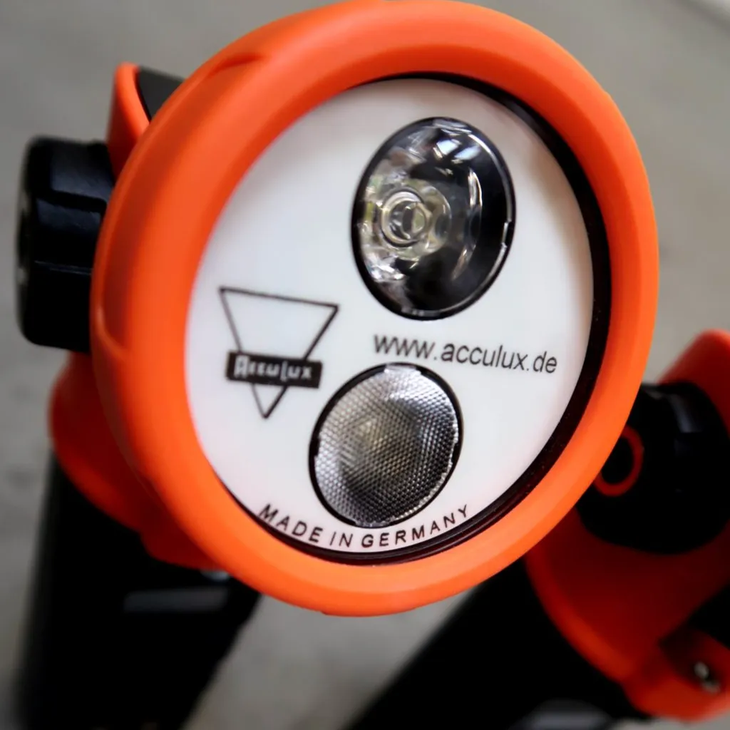 Close-up van een oranje-witte Acculux-zaklamp met lens en LED-lampje, waarop de website www.acculux.de en de tekst ‘Made in Germany’ op de voorkant te zien zijn.
