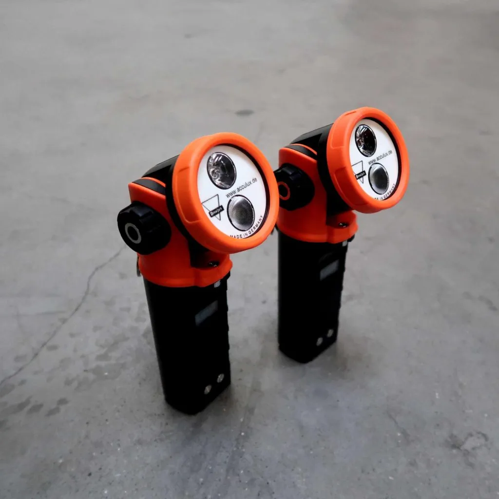 Twee oranje en zwarte handapparaten met twee ronde lampjes en draaiknoppen aan de zijkant staan rechtop op een grijs betonnen oppervlak.